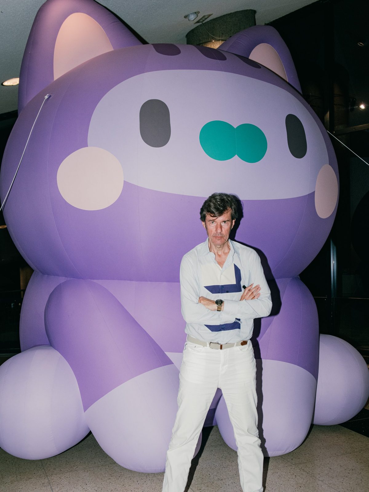 A man with crossed arms standing in front of the giant purple inflatable cat at night