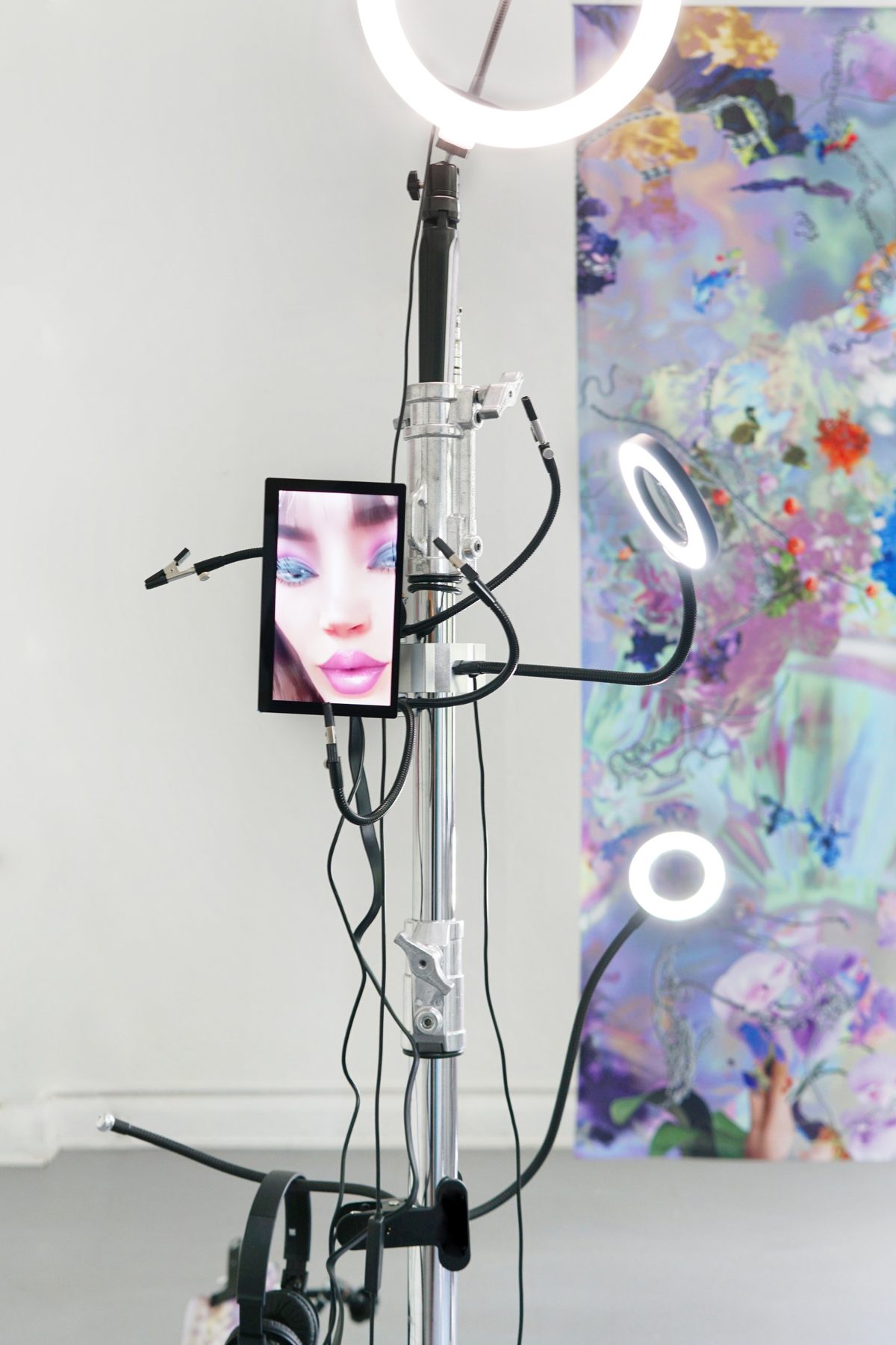 Close-up of the light stand: ring lights on gooseneck arms and a small screen with a glossy pink-lipped face