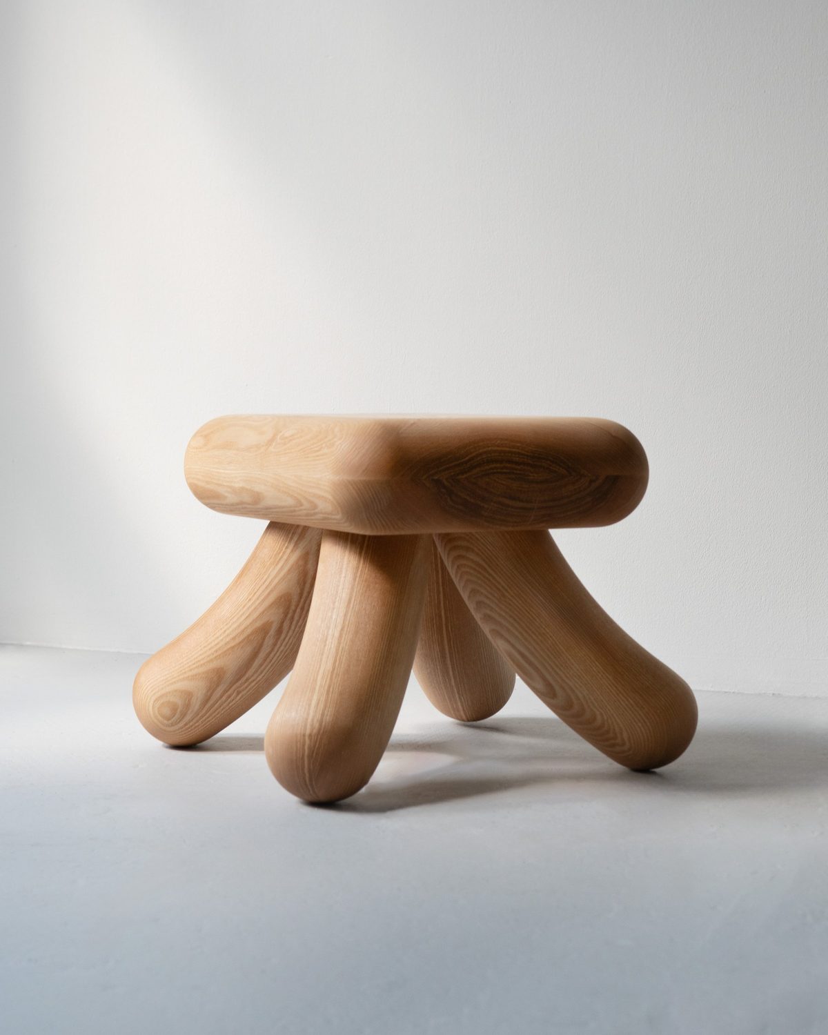 Kanji-Stool from a three-quarter view, four rounded legs splaying out from a cushion-like seat