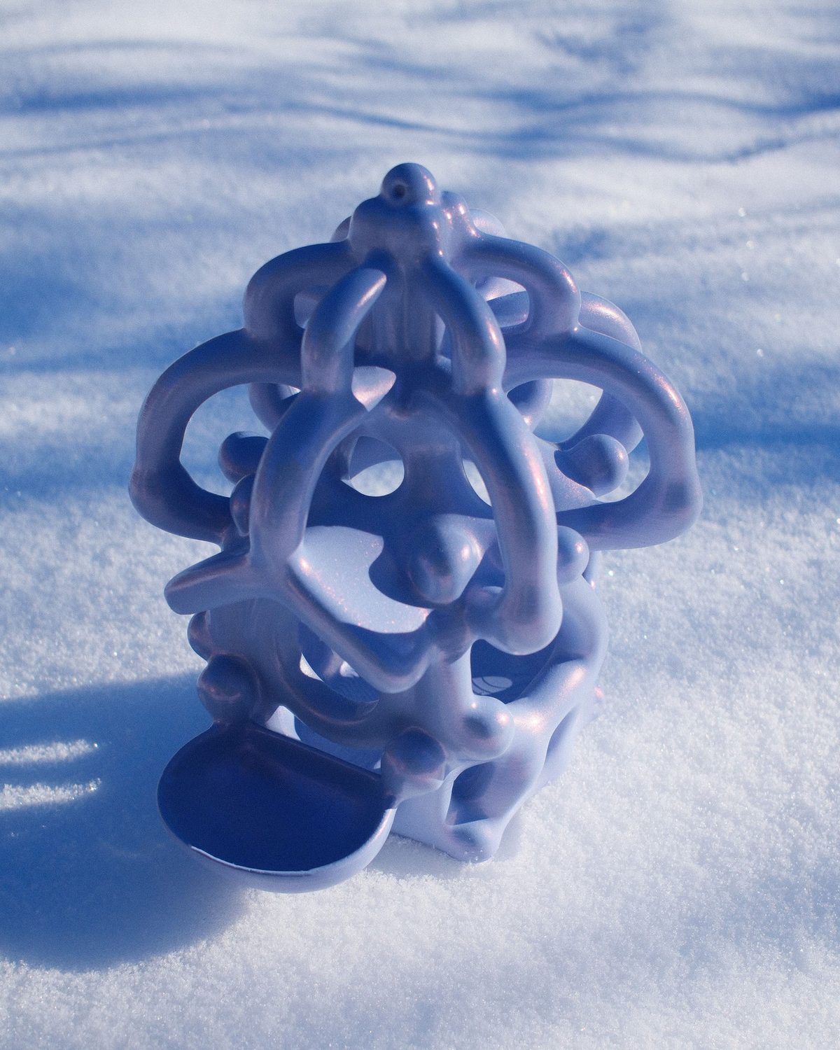 The lilac birdhouse standing in deep snow, its feeding bowl in the sun
