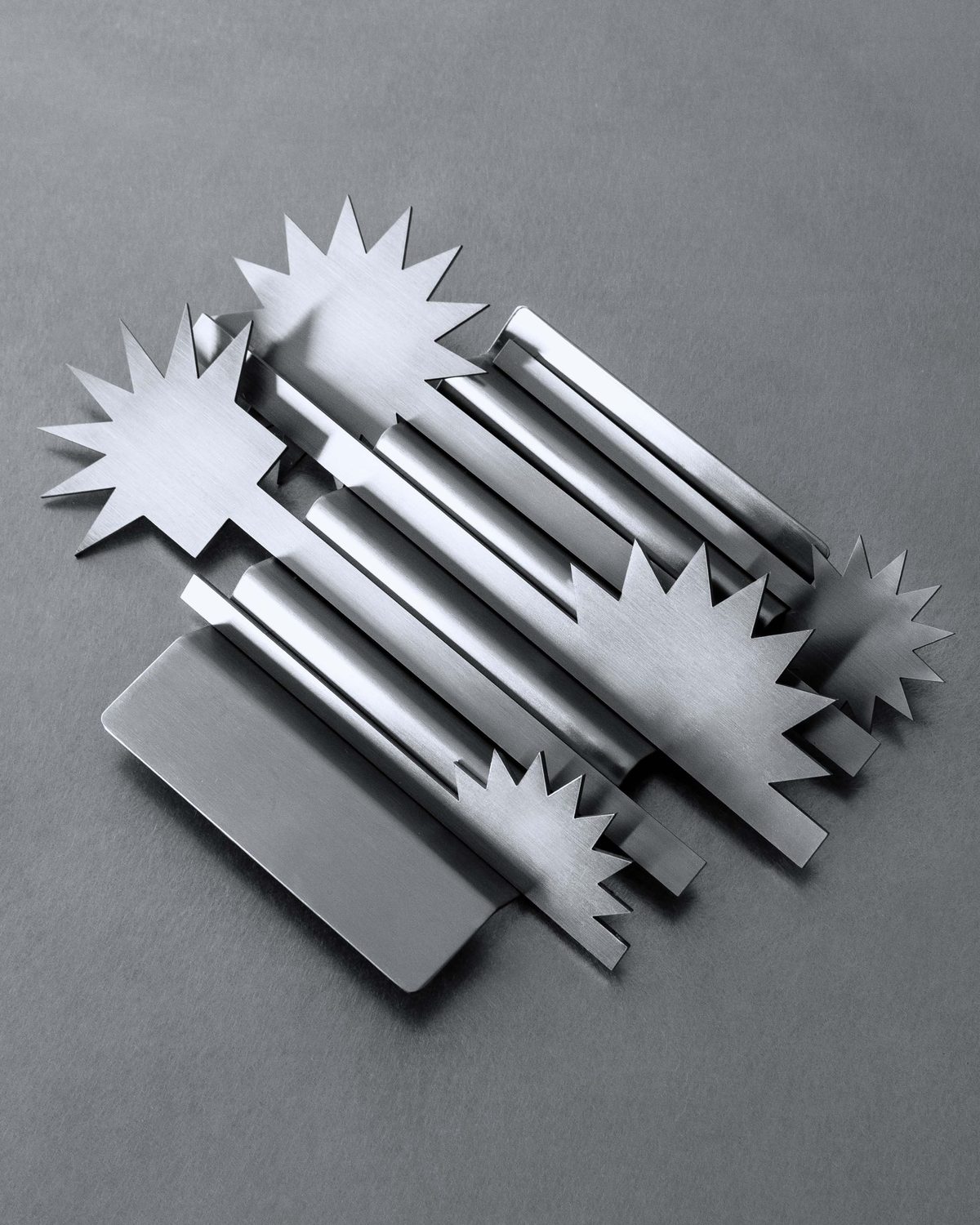 The full Spikey set of brushed steel pieces with star-shaped ends, laid out on grey paper