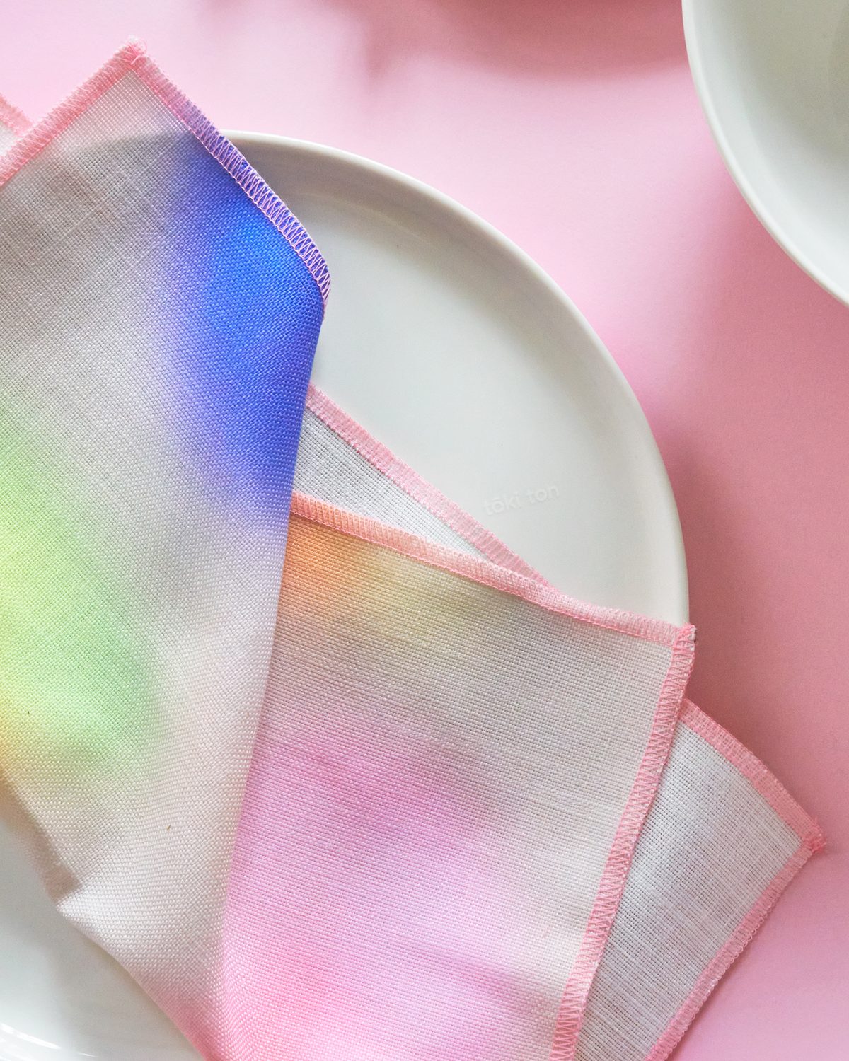 Close-up of folded linen napkins with blue, green and pink gradients on a white plate