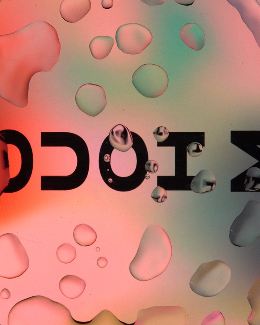 Film still: the word TOCA ME seen through drops and blobs of liquid on a pink and mint gradient