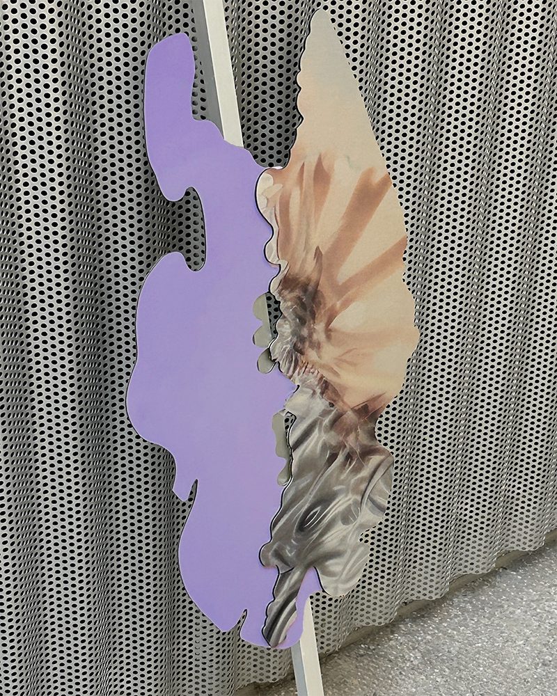 A wavy cut-out object, half lilac, half printed with a pale flower, leaning against a perforated metal wall
