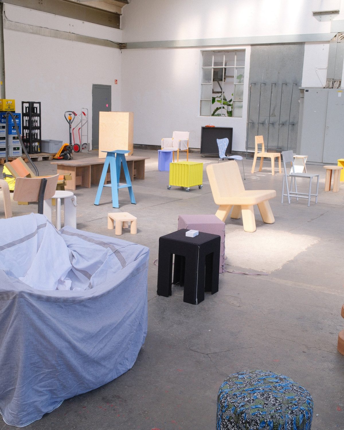 Colourful stools and chairs in the sunlit hall, a fabric-covered chair in the foreground