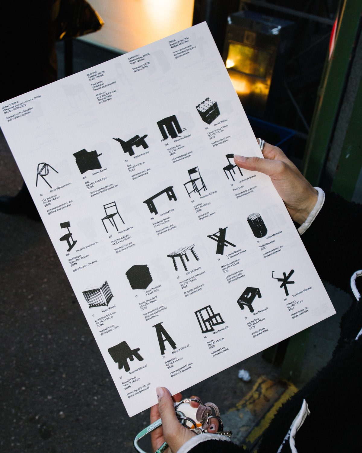 Hands holding the riso-printed exhibition sheet with black silhouettes of all the seats